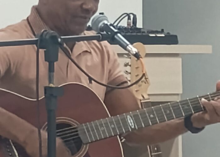 Homem pele negra camisa marrom, sentado tocando violão