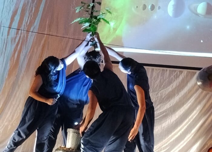 Quatro pessoas com roupas pretas, formando um circulo, segurando no alto uma planta