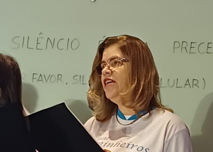 Mulher pele branca, cabelo loiro, óculos, camisa branca, segurando uma pasta,