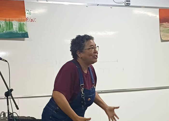 Mulher branca, cabelo preto, óculos, camisa vinho, macacão azul.