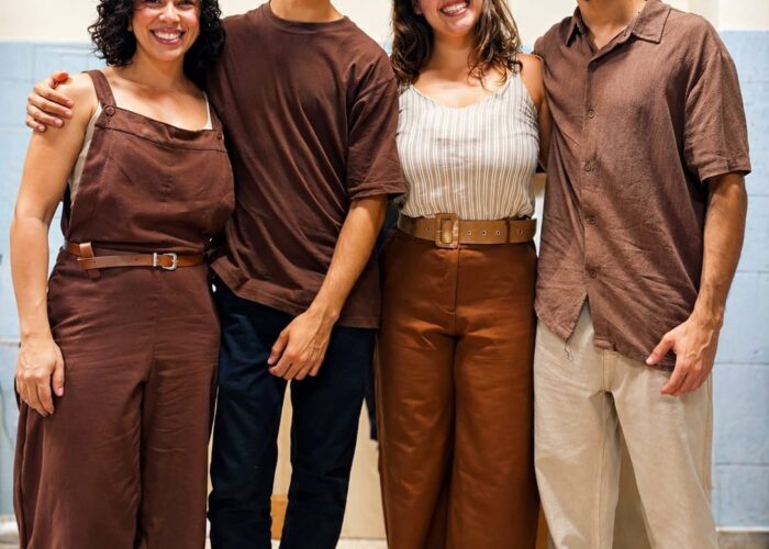 A esquerda mulher pele branca, cabelo preto, camisa e calça marrom, homem pele branca, cabelo preto, óculos, camisa marrom, calça preta, mulher pele branca, cabelo loiro, camisa branca, calça marrom, homem pele branca, cabelo preto, óculos, camisa marrom, calça bege.