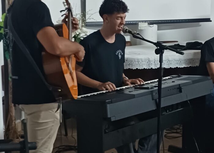 Rapaz pele parda, cabelo preto, camisa preta, calça bege, em pé tocando violão, rapaz pele branca, cabelo preto, camisa preta, sentado tocando teclado.